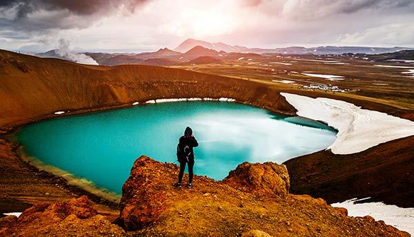 solo traveller on group tour to iceland standing over the blue lake myvtan with hills and steam and snow surounding