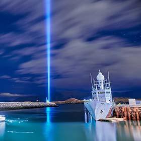 boats moored on lake with beam of blue light from imagine peace tower