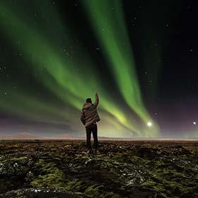 solo traveller standing with arm pointed to the sky showing northern lights aurora