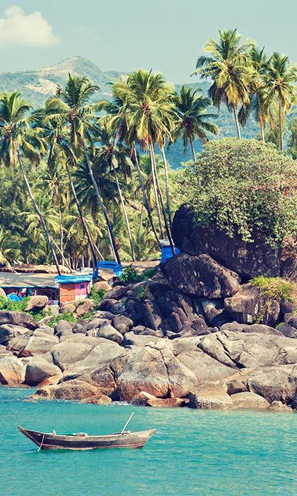 boat floating on clear blue sea against a rocky beach in goa on a group tour to india