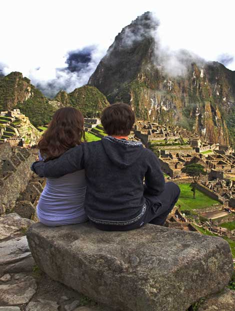 Couple of adventure travellers look in awe of their surroundings as they sit overlooking acient Machu Picchu ruins