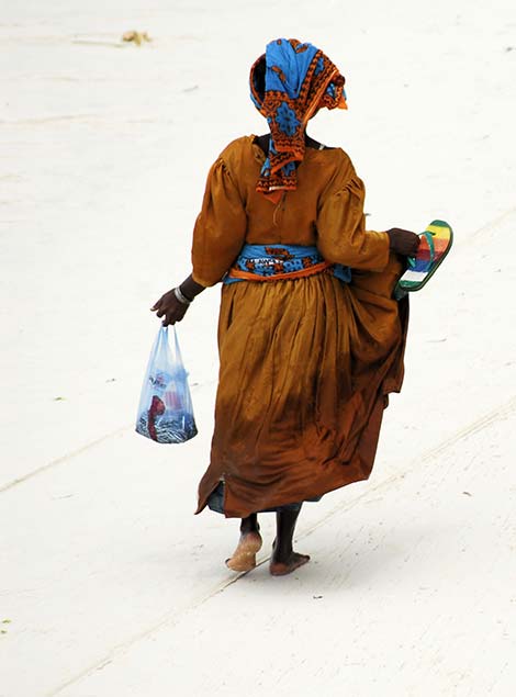 traditionally dressed tanzanian woman walking on the beach in zanzibar