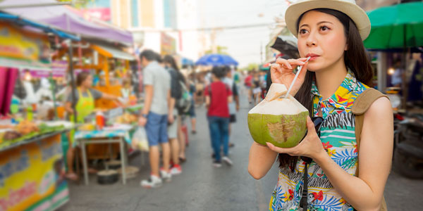 A traveller sipping on fresh coconut water in a market in Bangkok