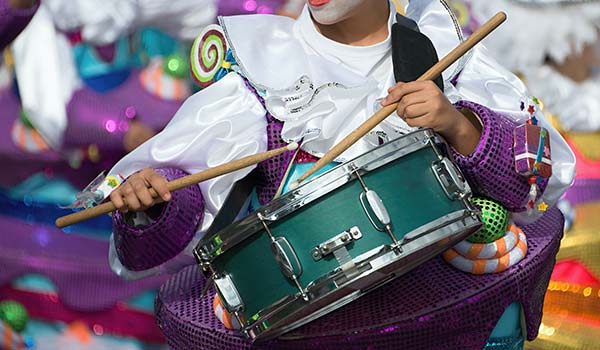 person dressed up as a minstrel playing a drum in purple clothing for the cape town minstrel festival in south africa