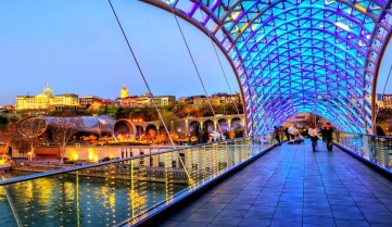 View over the modern glass Peace bridge to the President Palace and Trinity Cathedral on late evening, Tbilisi, Georgia
